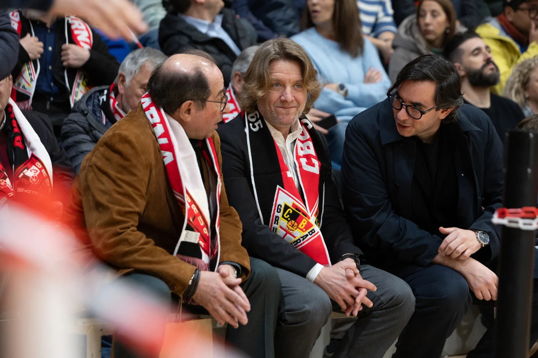 Three club directors wearing Barna scarves, watching the game from the stands at La Nau