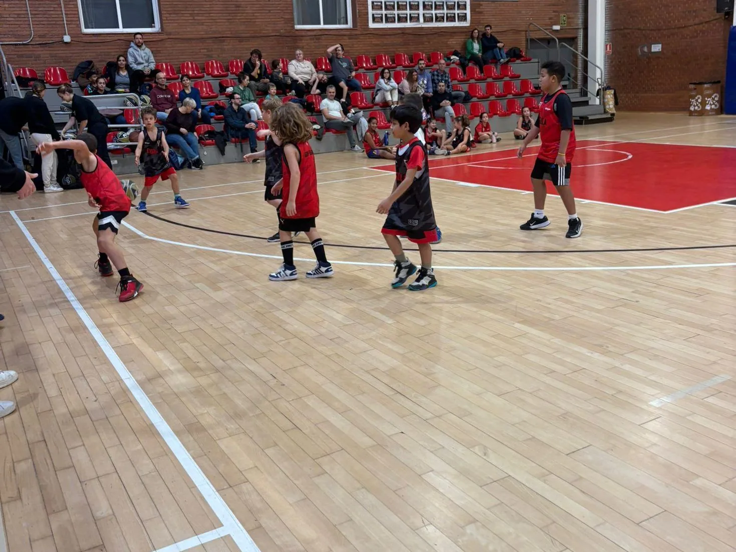 Entrenament de l'Escola de Bàsquet del CB Grup Barna a la pista, amb famílies a la grada